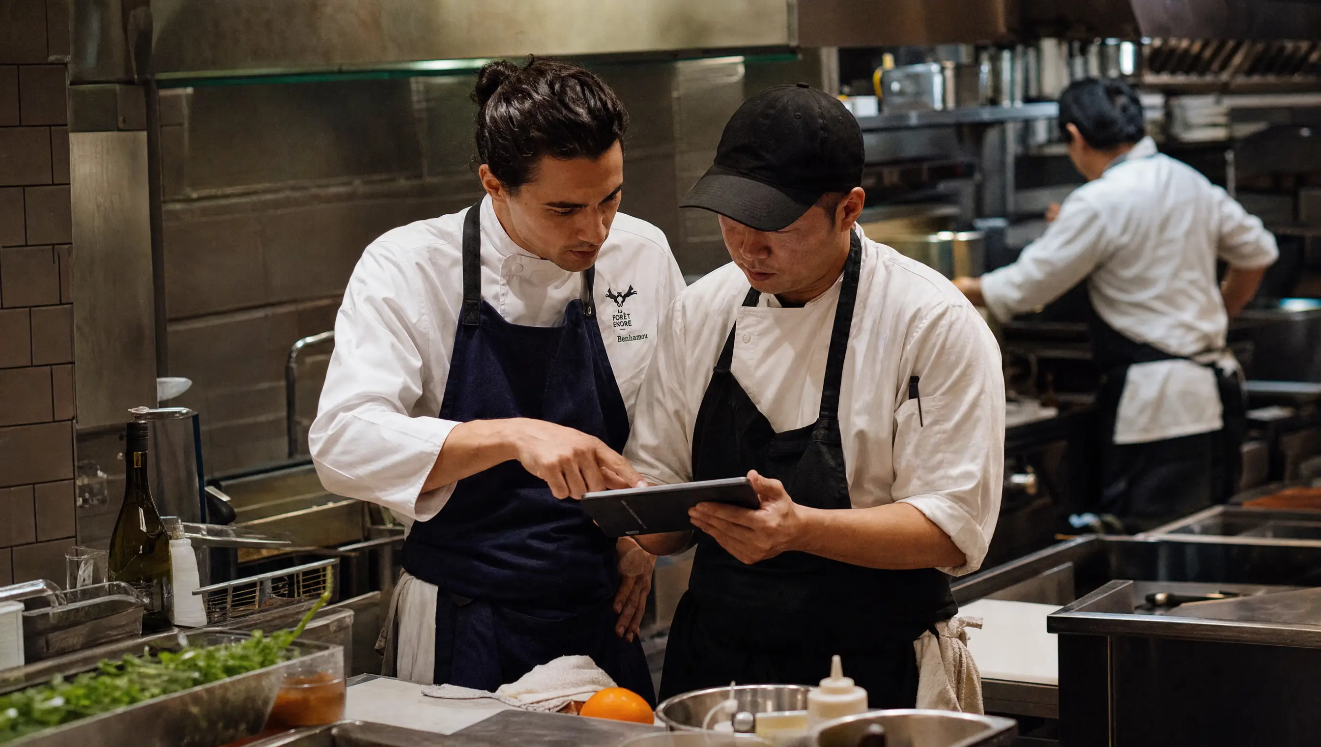 Dos personas del equipo de cocina repasando la carta en una tablet junto al pase